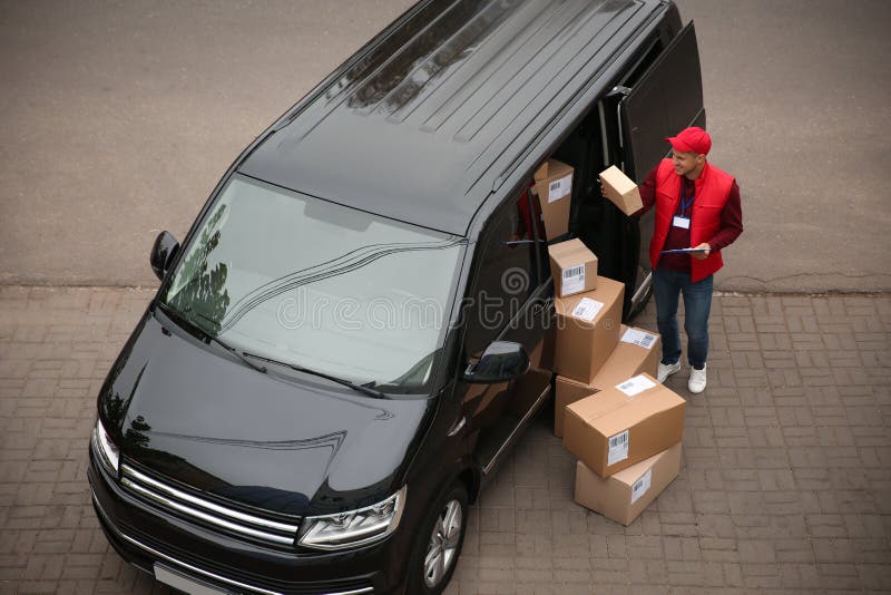 Courier with clipboard and parcels near delivery van outdoors, above view stock image