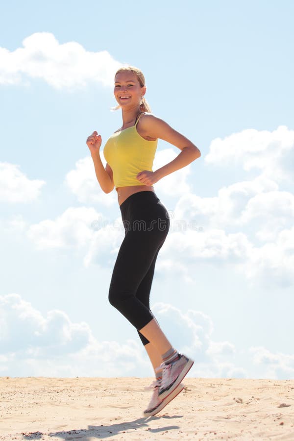 Woman wearing jogging attire on sand with a blue cloudy sky in the background. Woman wearing jogging attire on sand with a blue cloudy sky in the background.