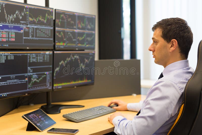 Stock broker trading online while accepting orders by phone. Trader`s office with multiple computer screens full of index charts and data analyses. Stock broker trading online while accepting orders by phone. Trader`s office with multiple computer screens full of index charts and data analyses.