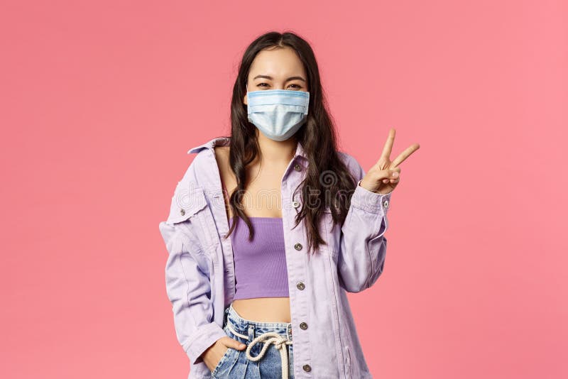 Covid19,隔离,人的概念 乐观,微笑的快乐女孩戴着医用面罩,在家里展示和平标志 库存照片 Covid19,隔离,人的概念 乐观,微笑的快乐女孩戴着医用面罩,在家里展示和平标志 库存照片