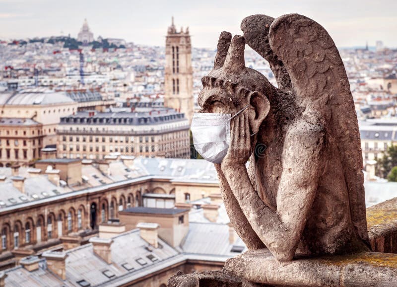 COVID-19 coronavirus in France, medical mask on gargoyle of Notre Dame in Paris. Tourist landmarks closed due to corona virus