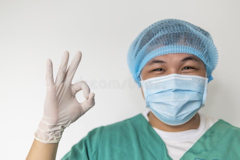 Happy male doctor with medical mask in hospital showing ok hand sign, safety sign