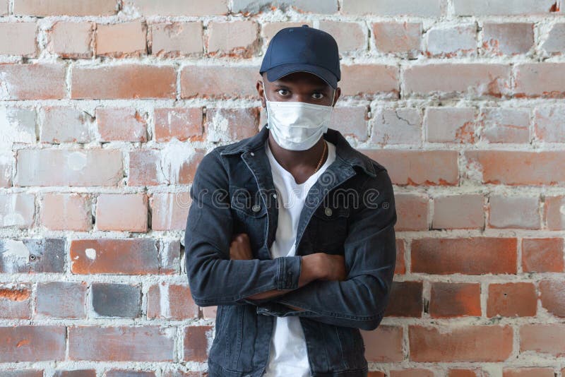 Covid covid19 Coronavirus pandemischer junger afrikanischer schwarzer Mann, der medizinische Maske wird, steht in einer Mütze mit lizenzfreie stockfotos