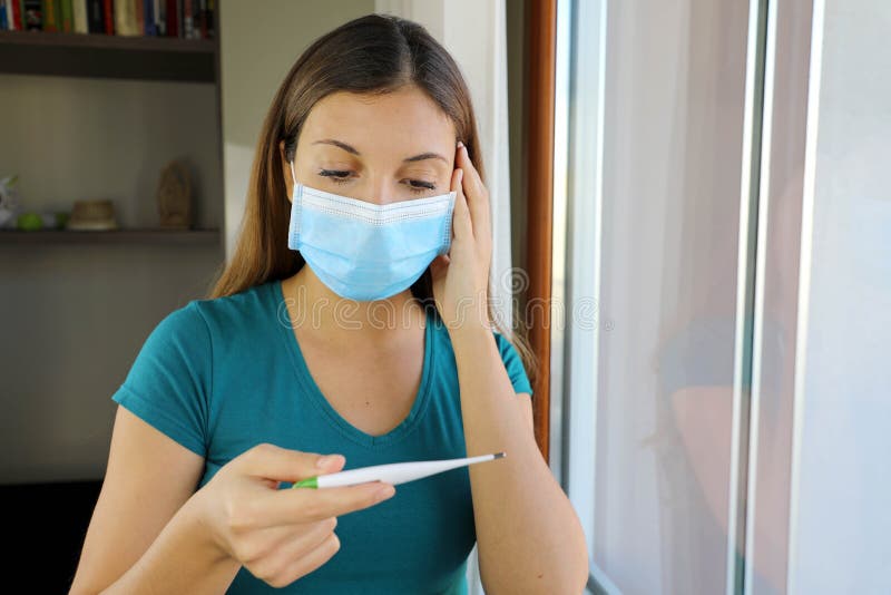 COVID-19 Pandemic Coronavirus Surgical Mask Woman Checking Temperature with Thermometer at Home Symptom of SARS-CoV-2. Girl with