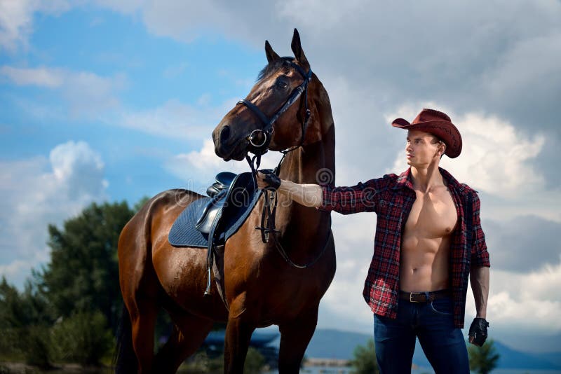 Cowboy bello e cavallo dell'uomo macho sui precedenti del cielo e dell'acqua