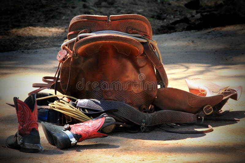 Western cowboy equipment. Saddle boots rope and breast collar laying on the ground. Possible flyer or brochure background.