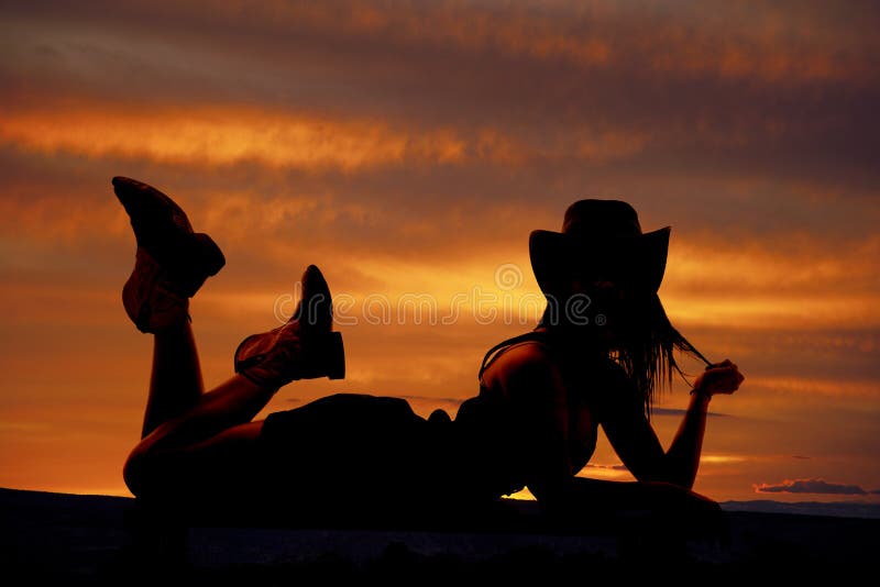 A silhouette of a cowgirl is laying on her stomach. A silhouette of a cowgirl is laying on her stomach.