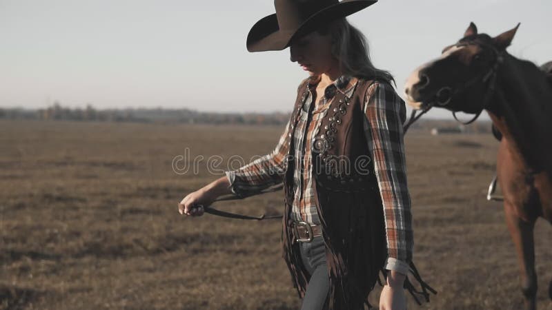 Cowgirlen som tar på, går hennes mörka häst vid tömmar på soluppgång Väldigt gå för häst