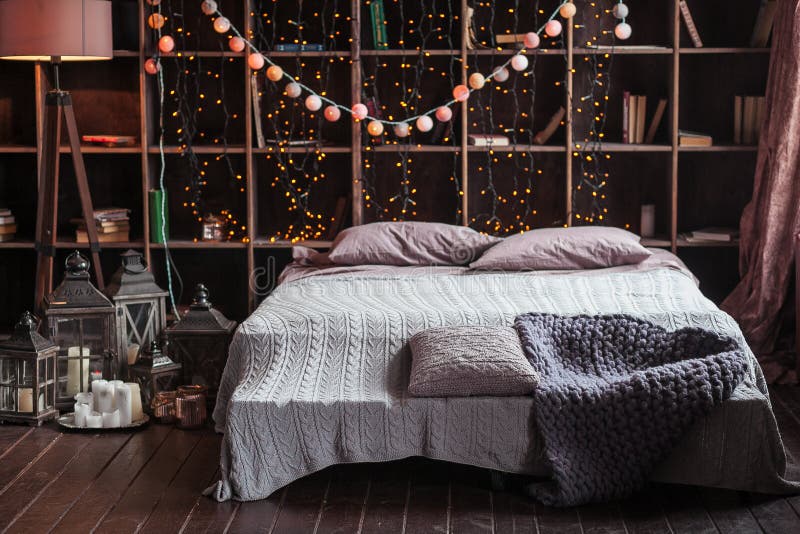 Coziness, comfort, interior and holidays concept - cozy bedroom with bed and garland lights at home. A rack with books