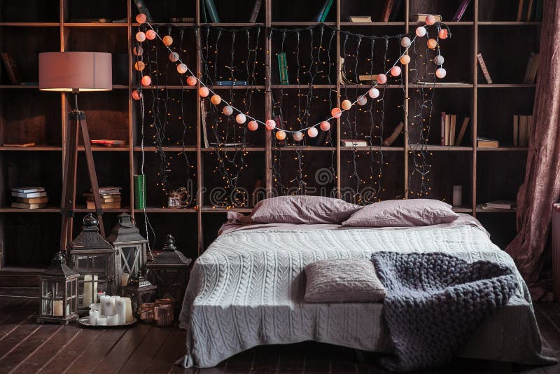 Coziness, comfort, interior and holidays concept - cozy bedroom with bed and garland lights at home. A rack with books