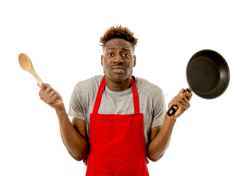 Cozinheiro afro-americano preto da casa do homem no avental do cozinheiro chefe que cozinha a bandeja e a colher perdidas e sobre fotografia de stock Cozinheiro afro-americano preto da casa do homem no avental do cozinheiro chefe que cozinha a bandeja e a colher perdidas e sobre fotografia de stock