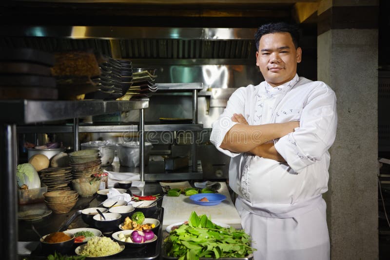 Cozinheiro chefe asiático que sorri na câmera na cozinha do restaurante