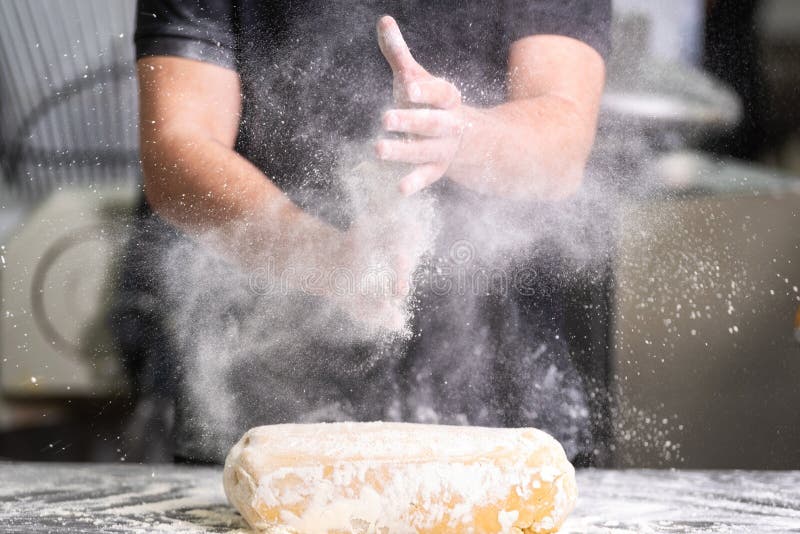 Cozinheiro chefe de pastelaria que aplaude suas mãos com farinha ao fazer a massa