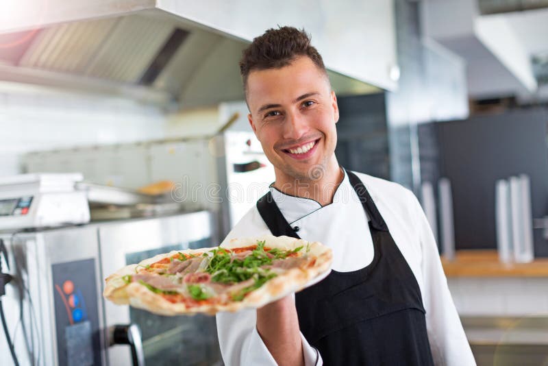 Cozinheiro chefe de sorriso que guarda a pizza fresca na cozinha