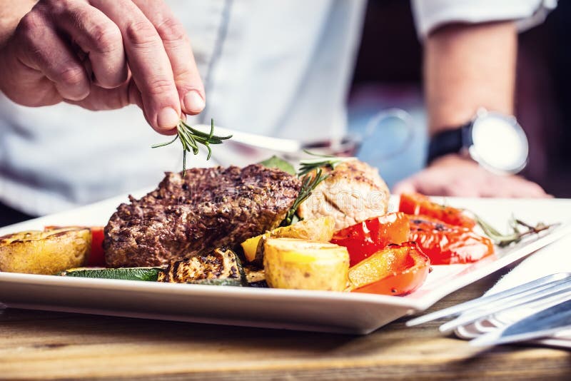 Cozinheiro chefe na cozinha do hotel ou do restaurante que cozinha somente as mãos Bife preparado com decoração vegetal Cozinheiro chefe na cozinha do hotel ou do restaurante que cozinha somente as mãos Bife preparado com decoração vegetal