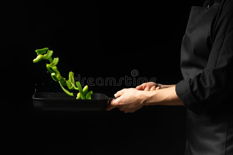 Cozinheiro profissional Prepara um prato com pimentas doces verdes em uma caçarola no fundo preto, menu, livro da receita, alimen foto de stock Cozinheiro profissional Prepara um prato com pimentas doces verdes em uma caçarola no fundo preto, menu, livro da receita, alimen foto de stock