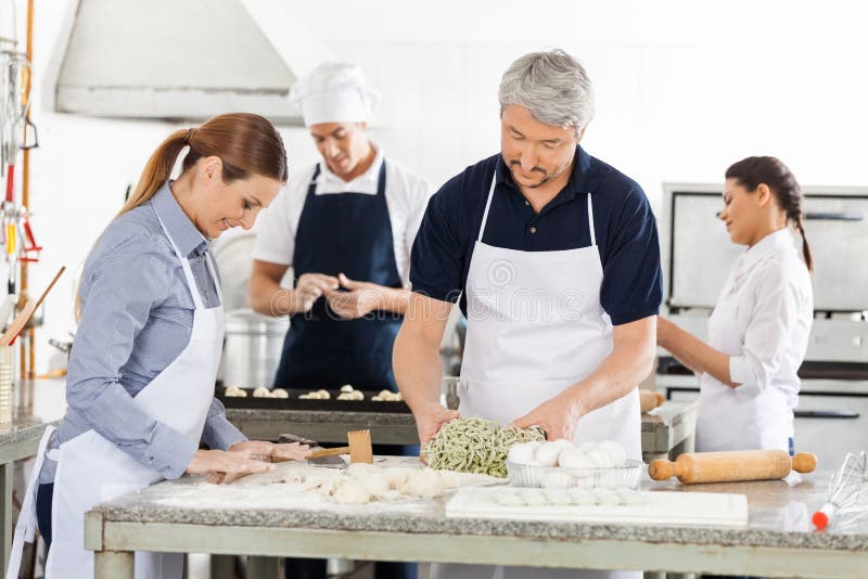 Cozinheiros chefe que preparam a massa junto na cozinha imagem de stock royalty free Cozinheiros chefe que preparam a massa junto na cozinha imagem de stock royalty free