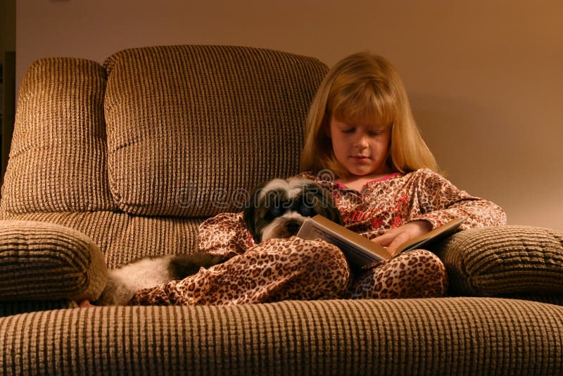 Una bambina rannicchiata su una sedia comoda, prima di andare a letto con il suo cane e un libro preferito.