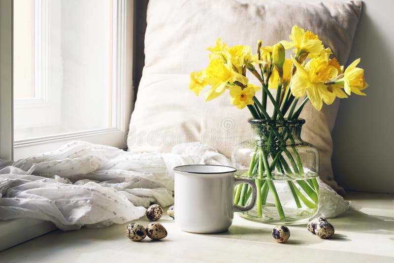 Cozy Easter, spring still life scene. Mug of coffee, wooden plate, quail eggs and vase of flowers on windowsill. Floral