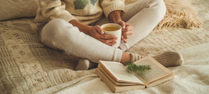 Cozy home. Beautiful girl is reading a book on the bed. Good morning with tea. Pretty young girl relaxing. The concept of reading