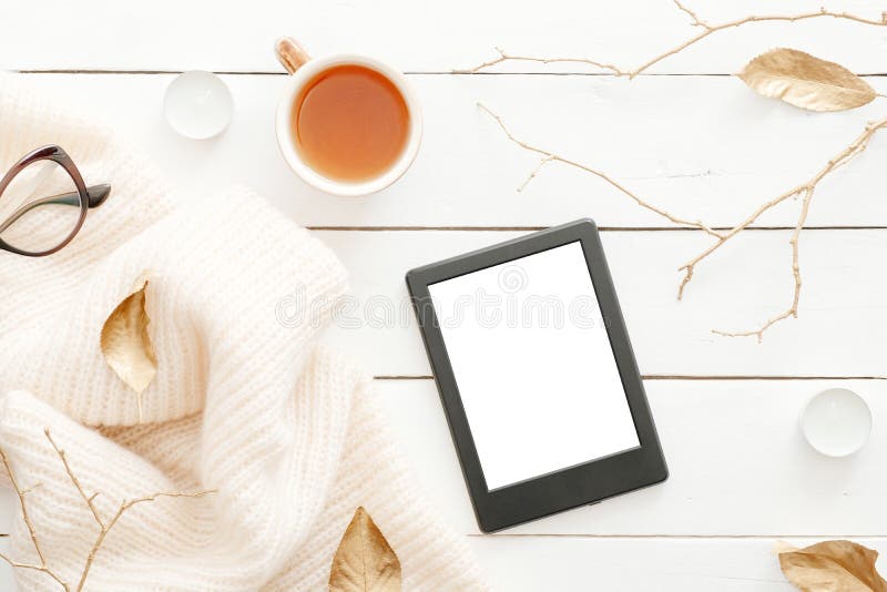 Cozy home desk table with knitted plaid, tea cup, fall leaves, tablet with blank screen on wooden white background. Top view, flat