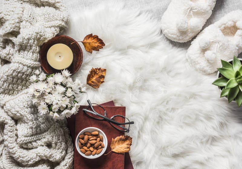 Cozy home interior in scandinavian style - stack of books, almond nuts, knitted plaid, succulentus flower, candle, chrysanthemum