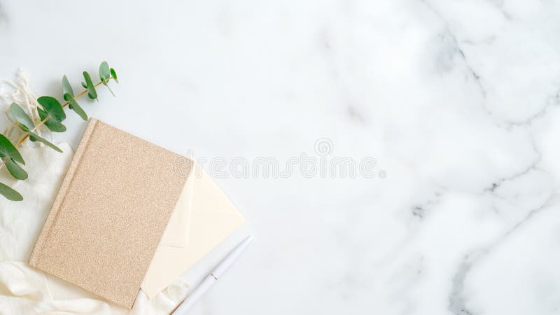 Cozy home office desk table with paper notebook, pen, eucalyptus leaf on marble background. Top view, flat lay, copy space.