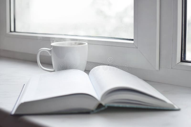Cozy home still life: cup of hot coffee or tea and opened book on windowsill. Education concept, free copy space