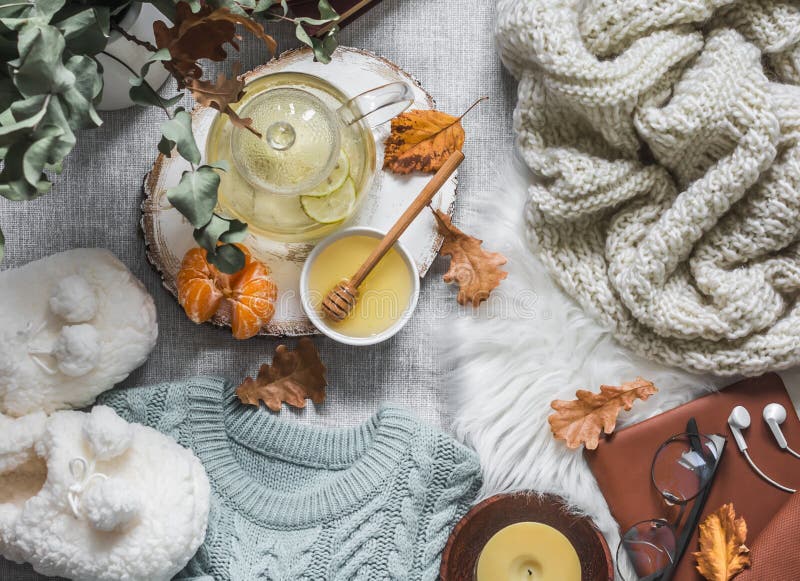 Cozy home still life - soft slippers, knitted sweater, plaid, green tea with honey, tangerines, books on a light background, top