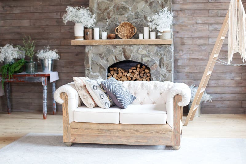 Cozy Interior living room white Sofa and Fireplace. Rustic Home Design for Warm Indoor Space Alpine Vacation. Modern Cottage Living Room Decor with Wood Wall and Furniture. Scandinavian style. Bohon
