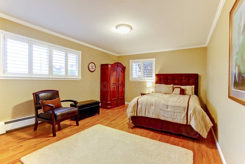 Cozy large guest room with suede brown bed and armor, hardwood floors and beige walls.