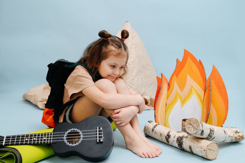 Cozy little girl sitting next to a fake campfire, hugging her knees