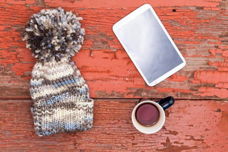 Cozy winter cap, tablet and tea on a grungy table