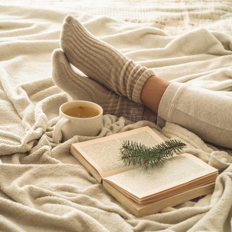 Cozy winter evening , warm woolen socks. Woman is lying feet up on white shaggy blanket and reading book. Cozy leisure scene