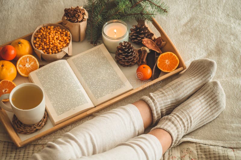 Cozy winter evening , warm woolen socks. Woman is lying feet up on white shaggy blanket and reading book. Cozy leisure scene