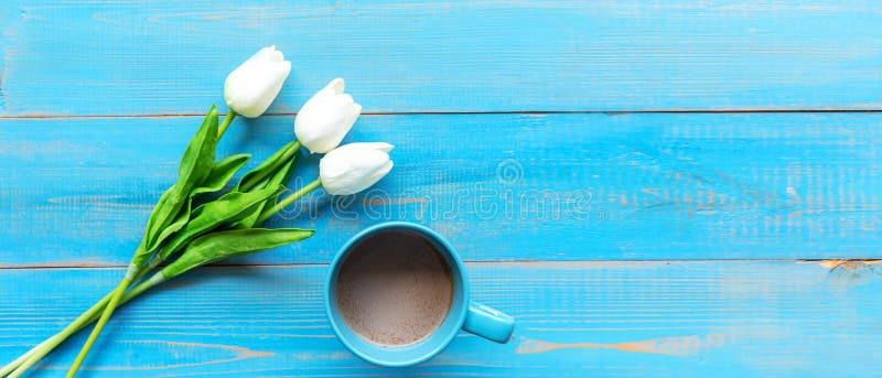 Cozy winter relax time.  Cup of hot coffee with tulip flower on the blue wood background