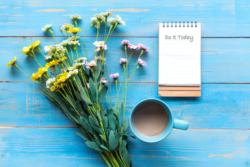 Cozy winter relax time.  Cup of hot coffee with write note on paper and flower on the blue wood background