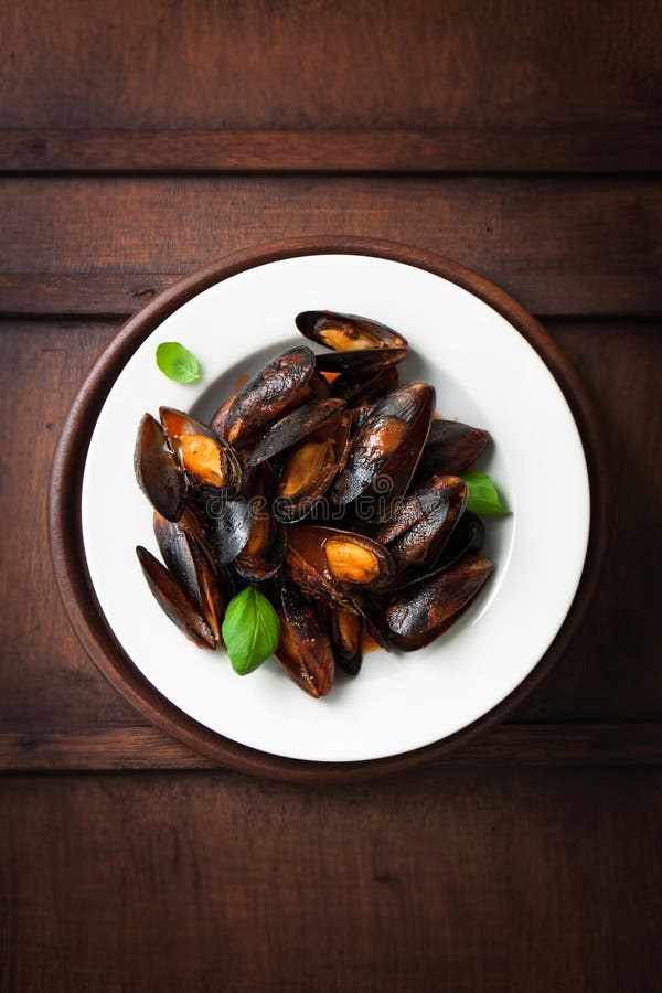 Cozze cucinate casalinghe con aglio, salsa al pomodoro, le erbe italiane, il vino bianco ed il basilico fresco in un piatto immagini stock Cozze cucinate casalinghe con aglio, salsa al pomodoro, le erbe italiane, il vino bianco ed il basilico fresco in un piatto immagini stock