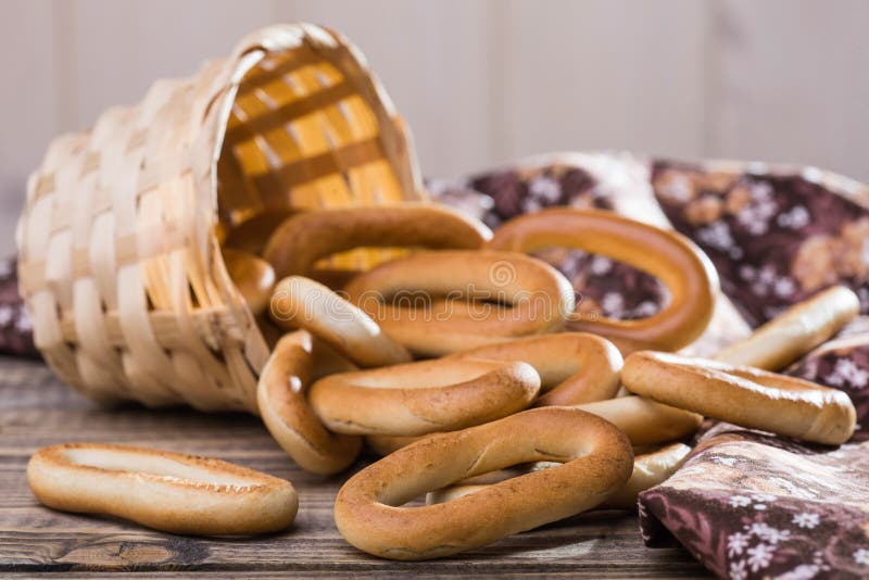 Photo still life closeup basket lying sidelong with delicious hard oval cracknels poured out on wooden table near flowery cloth over blurred rustic background, horizontal picture. Photo still life closeup basket lying sidelong with delicious hard oval cracknels poured out on wooden table near flowery cloth over blurred rustic background, horizontal picture