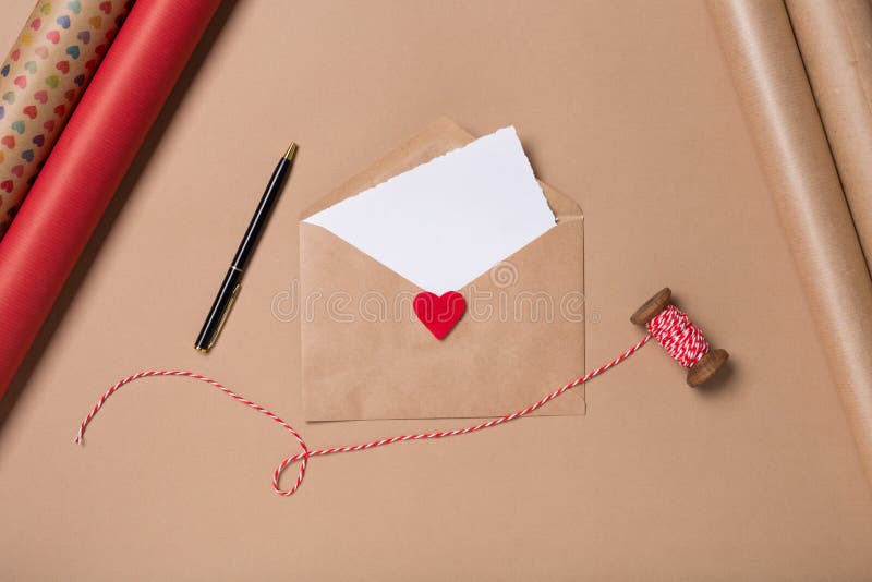 Craft envelope with blank paper, pen and red heart on beige background. Love concept. Saint Valentine`s Day concept