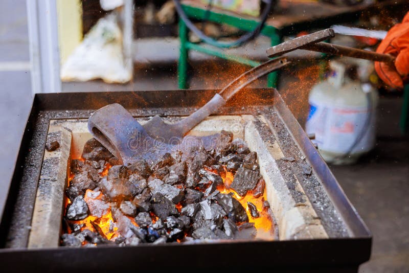 Craftsman actively shaping metal axe while working in forge with glowing coals sparks flying stock images