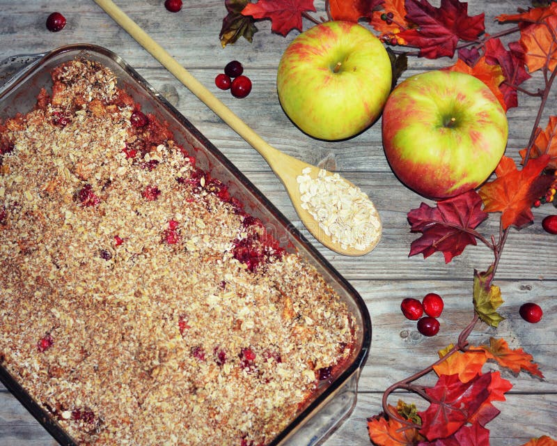 A 9x13 pan of cranberry apple cobbler with a wooden spoon filled with oatmeal and cranberries and apples and fall leaves framing the delicious dish.