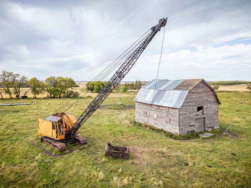 A crane is lifting a large object in front of a dilapidated barn stock photo