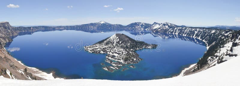 Clear blue water of Crater Lake National Park in Oregon during early spring with some snow left from winter. Wizard Island in the distance. Clear blue water of Crater Lake National Park in Oregon during early spring with some snow left from winter. Wizard Island in the distance.