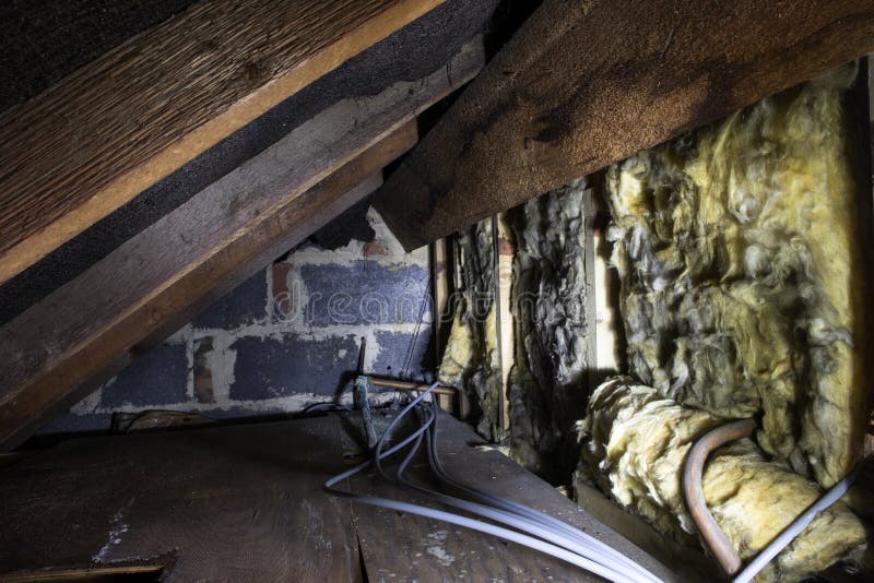 Crawl space under the eves of a house showing old fibreglass insulation, pipework, rafters, breezeblock construction and old board