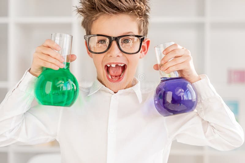 Excited little boy with glasses screaming and presenting flasks with bright liquid while conducting experiment during chemistry lesson in contemporary school. Excited little boy with glasses screaming and presenting flasks with bright liquid while conducting experiment during chemistry lesson in contemporary school