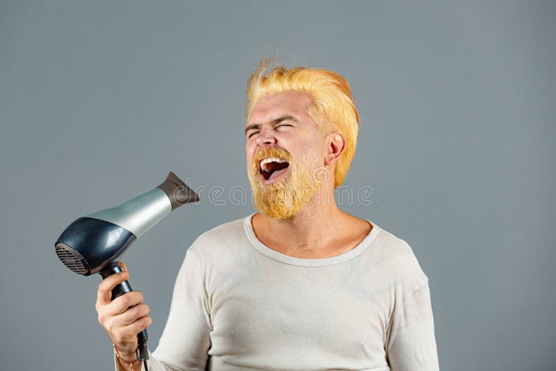 Crazy stylish man. Drying hair of a young funny amazed excited bearded man. Blonde beard man with hair dryer. stock image