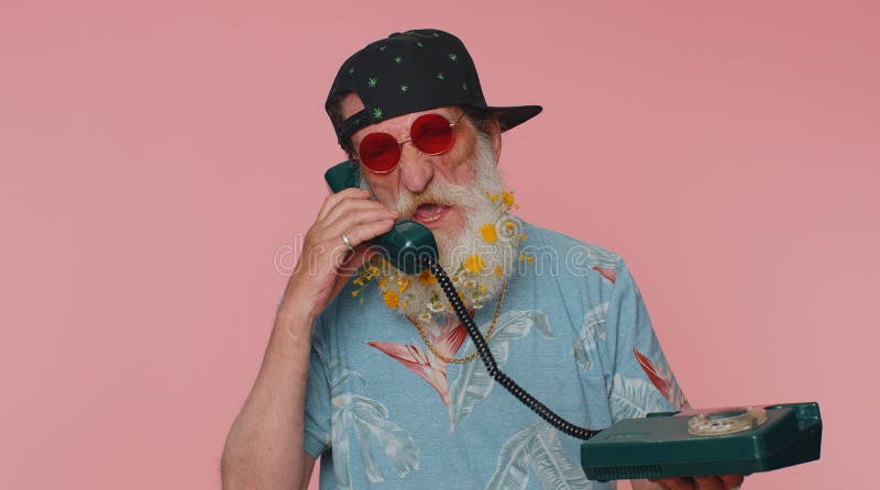 Crazy stylish senior old man talking on wired vintage telephone of 80s, fooling, making silly faces royalty free stock photos