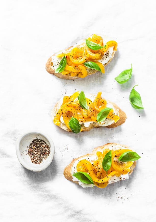 Cream cheese, roasted yellow bell pepper, basil bruschetta on on light background, top view. Copy space