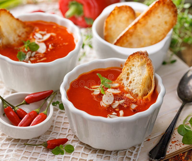 Cream soup van geroosterde peper waaraan amandelvlokken, Spaanse peper, verse kruiden en gisten zijn toegevoegd in een witte kera stock afbeeldingen Cream soup van geroosterde peper waaraan amandelvlokken, Spaanse peper, verse kruiden en gisten zijn toegevoegd in een witte kera stock afbeeldingen